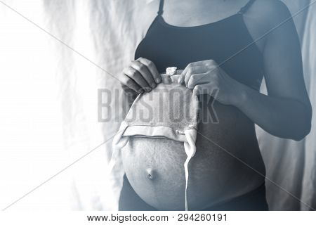 Close Up View Of Nacked Belly Of Pregnant Woman Holding Baby Boy Hat. Pregnant Woman Is Holding A Sm