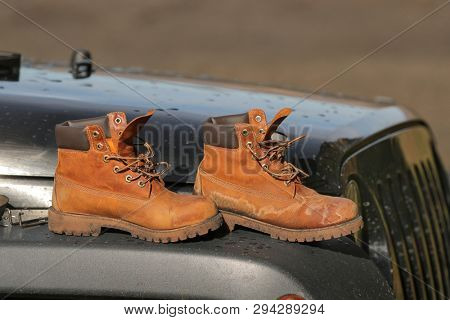 Clened boots air drying in the sun o nthe front of a four wheel drive off-road car on a road trip