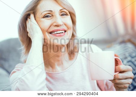 A Woman Over 50 Years Of European Appearance Resting At Home Drinking Coffee. The Woman Smiles Broad