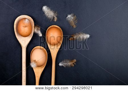 Fresh chicken eggs in wooden spoons and fethers. Kitchen utensil for cake, pastry or cookies on backboard background. Top view with copy space.