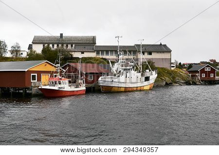 Two Small Boats At Reine Harbor In Front Of Traditional Wooden Fishing Cabins On Lofoten Islands In 