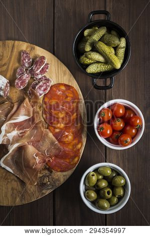 Selection Of Charcuterie And Tapas Dishes On A Wooden Table, Including Meat And Chorizo, Gherkins, C