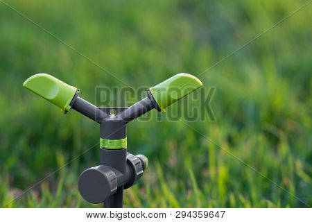 Two Arm Green Rotating Sprinkler On Spike On Fresh Spring Grass Background. Copy Space. Selected Foc