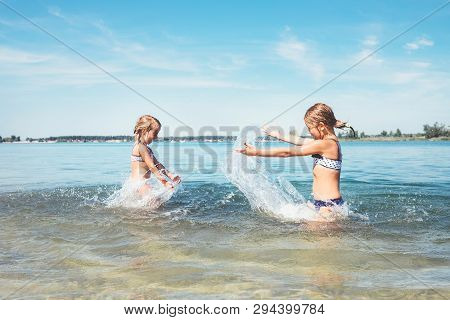Two Little Sister Girls Fooling Around In The Calm Sea Waves Splashing Water To Each Other. Family V