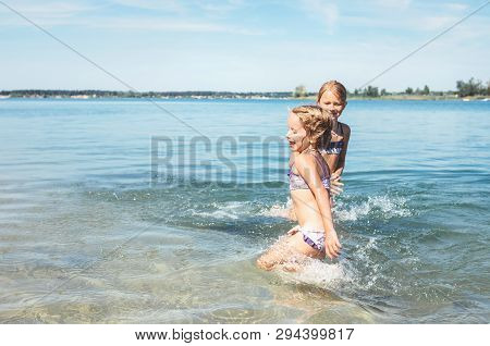 Two Little Sister Girls Fooling Around In The Calm Sea Waves Splashing Water To Each Other. Family V
