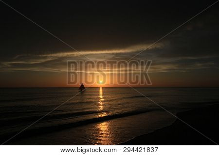 Captiva Island, Florida 08-05-2015 Small Sailboat In Partial Silhouette Against The Setting Sun In T