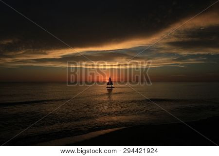Captiva Island, Florida 08-05-2015 Small Sailboat In Partial Silhouette Against The Setting Sun In T