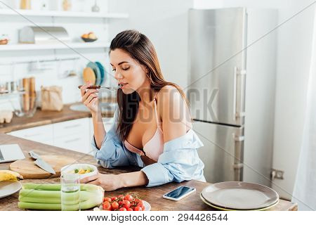 Sexy Girl In Bra And Shirt Eating Fruit Salad In Kitchen