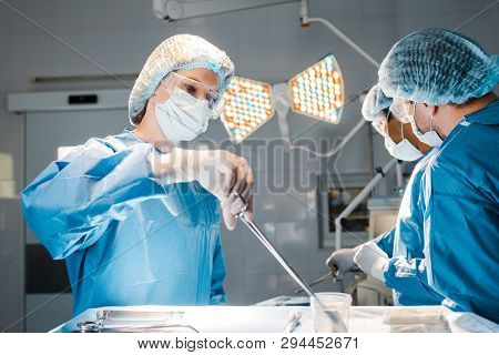 Doctors Doing Operation And Nurse In Uniform And Medical Cap Holding Equipment