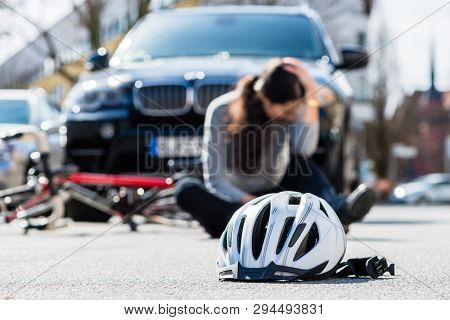 Bicycling helmet on the asphalt after accidental collision between the bicycle of a sorrowful young woman and a 4x4 car in the city