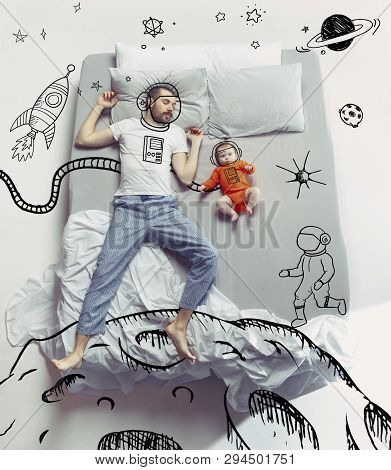 Conquerors Of Outter Space. Top View Photo Of Young Man And His Child Sleeping In A Big White Bed. D