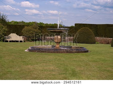 Stone Water Fountain On Grass With Wall And Bench In Background