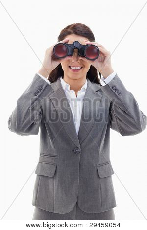 Close-up of a smiling businesswoman looking through binoculars against white background