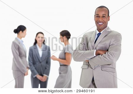 Close-up of a businessman smiling and crossing his arms with three female co-workers talking in the background