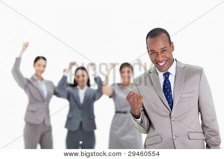 Close-up of a successful business team with man in foreground smiling and clenching his fist with three co-workers raising their arms