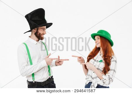 Happy young couple wearing costumes, celebrating St.Patrick 's Day isolated over white background, pointing fingers