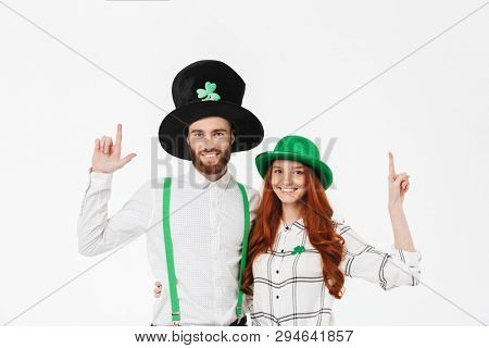 Happy young couple wearing costumes, celebrating St.Patrick 's Day isolated over white background, pointing fingers