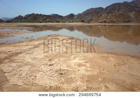 Desert landscape with cracked mud, puddle and dry mountains in Fujairah, United Arab Emirates