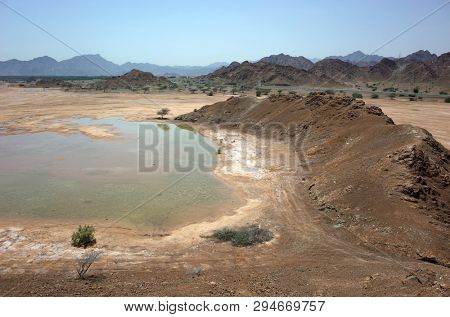 Arabian peninsula landscape with cracked mud, puddle and dry mountains in Fujairah, United Arab Emirates