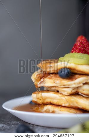 Someone Pouring Honey On Top Of Pancakes In White Ceramic Plate With Copy Space On The Left.
