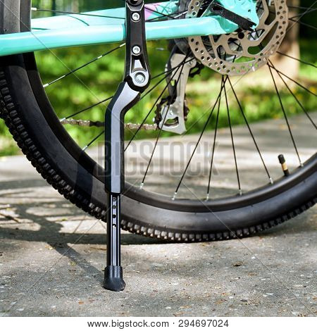 Bicycle Kickstand With Rear Bicycle Wheel Standing On The Asphalt With Green Grass On The Background