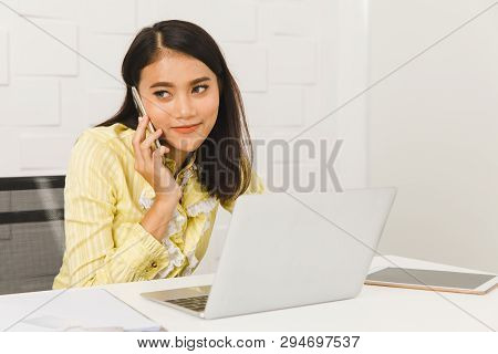 Young Beautiful Asian Architect In Business Casual, Busily Talking On Smartphone While Checking Deta