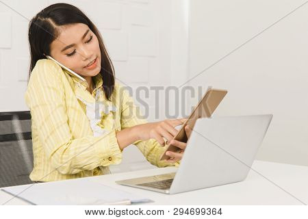 Young Beautiful Asian Architect In Business Casual, Busily Talking On Smartphone While Checking Deta