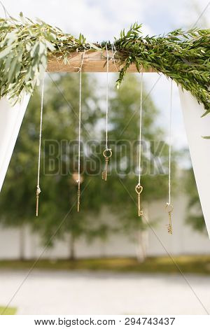 Metal Keys Hang On The Threads. Wedding Arch With Green Branches And White Cloth On A Blurred Backgr