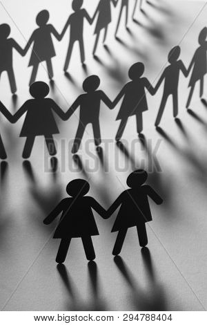 Black paper figure of a female couple in front of a crowd of paper people holding hands on white surface. Social movement, minorities, leadership concept.
