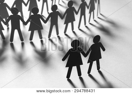 Black paper figure of a female couple in front of a crowd of paper people holding hands on white surface. Social movement, minorities, leadership concept.