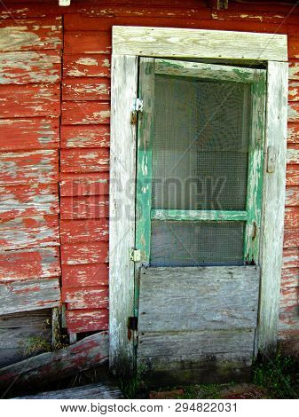Weathered, Old Front Door Of Shabby House With Red Peeling House Siding And Green Peeling Screen Doo