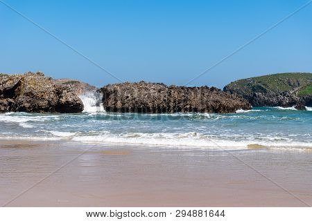 Scenic View Of Sand Beach With Rocks Against Blue Sky