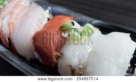 Closeup​ pieces​ of​ sushi​ with​ a variety of​ raw​ meat toppings​ on​ a plastic​ container.