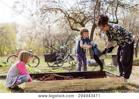 Mother with two young daughters gardening in urban community garden