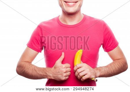 Smiling Handsome Guy Holding Yellow Banana And Showing Ok (thumb Up) Near His Stomach Over White Bac