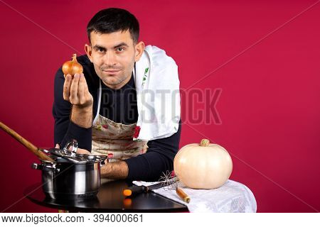 A Man Prepares Food At Home In The Kitchen And Poses With An Onion. Photo On A Pink Background With 
