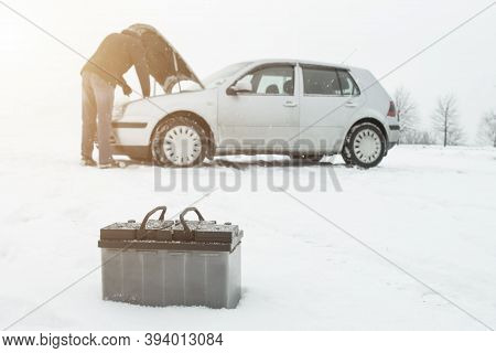 A Man Repairs A Car In Winter On Snow In The Background Is A Discharged Battery, Copy Space