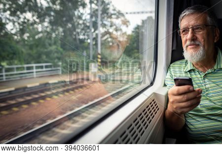 Senior man enjoying a train travel - leaving his car at home, he savours the time spent travelling, looks out of the window, has time to admire the landscape