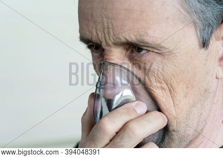 Medical Oxygen Mask On A Man. A Man Breathes Oxygen Using A Mask. Close-up Of An Old Man Doing Inhal