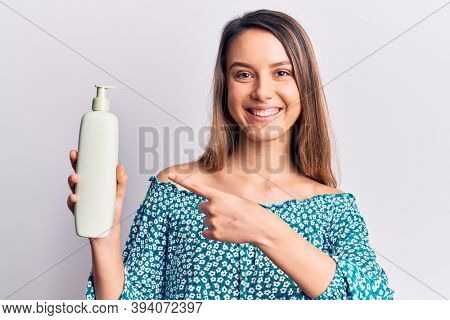 Young beautiful girl holding bottle of cream lotion smiling happy pointing with hand and finger 
