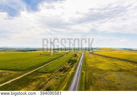 Aerial View Of The Highway Passing Through The Fields, And Wind Turbines. Shooting From A Drone.