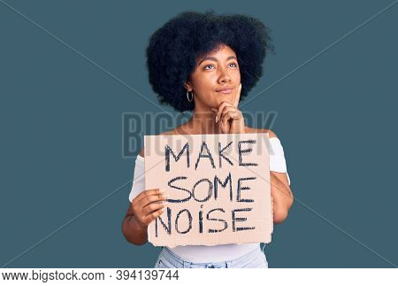Young african american girl holding make some noise banner serious face thinking about question with hand on chin, thoughtful about confusing idea 