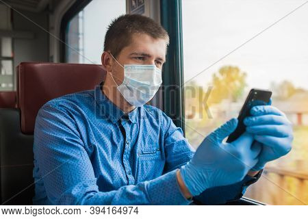 Young European Guy In A Blue Shirt, Protective Gloves And A Medical Mask With A Phone In His Hands M