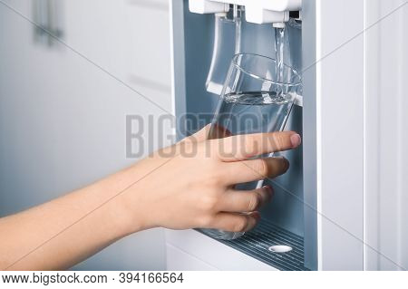 Woman Filling Glass With Water Cooler Indoors, Closeup. Refreshing Drink