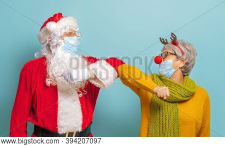 Merry Christmas and Happy Holidays! Santa Claus and reindeer on bright color background. Senior people in carnival costumes wearing face masks during Covid-2019