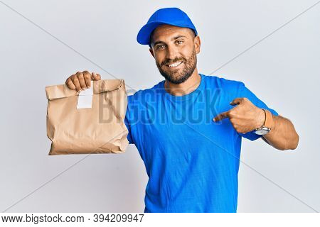 Handsome man with beard holding delivery package pointing finger to one self smiling happy and proud 