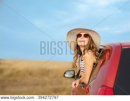 Cute Happy Smiling Little Girl Child Goes To Summer Travel Trip In The Red Car. Preteen In Hat And S
