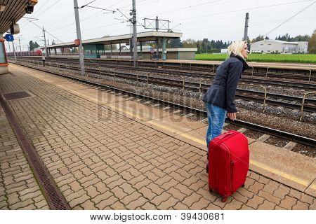 a young woman with luggage waiting on the platform of a railway station for their train. train delays