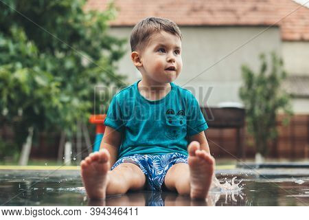 Adorable Caucasian Boy Lying On The Ground In Water Looking Happy At Something Wearing Blue Clothes