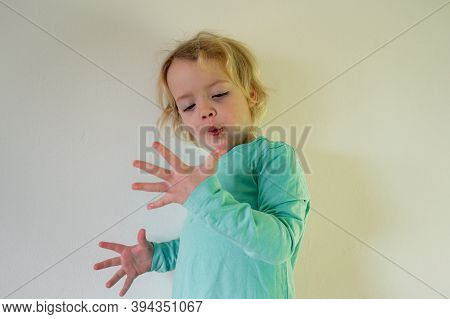 Portrait Of Cute Blonde Girl Wearing Cyan Shirt And Looking At Her Hand.